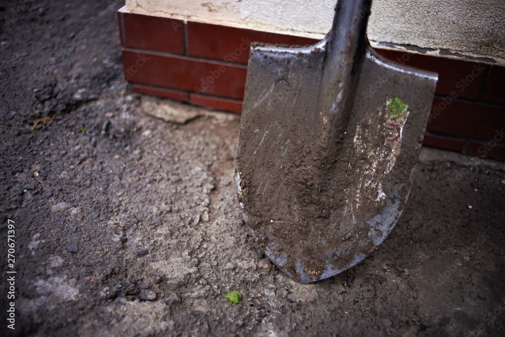 A shovel with stains of soil stands in an asphalt yard. Tool for garden works A shovel with stains of soil stands in an asphalt yard. Tool for garden works