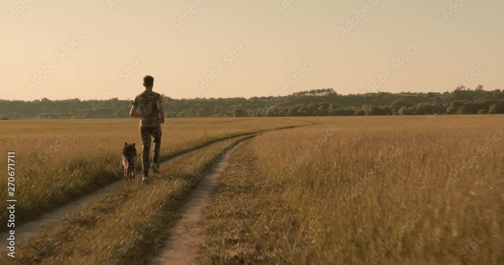 Teenager is running with a dog in nature while sunset. 15 year old boy with German shepherd runs on a countryside road. Teen on the field with dog. Guy is playing with his pet in meadow. Real time Teenager is running with a dog in nature while sunset. 15 year old boy with German shepherd runs on a countryside road. Teen on the field with dog. Guy is playing with his pet in meadow. Real time