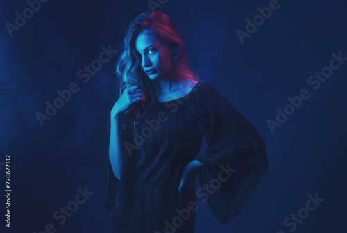 Beautiful ,young blonde with bright scarlet lips and expressive eyes in a black jumpsuit in neon light blue and red lamps.