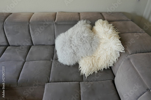 Two cuddly lambskin pillows on a gray velor sofa, close-up