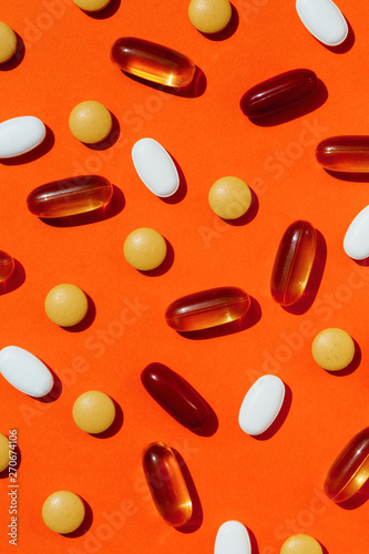 Scattered vitamins and fish oil capsules on an orange background