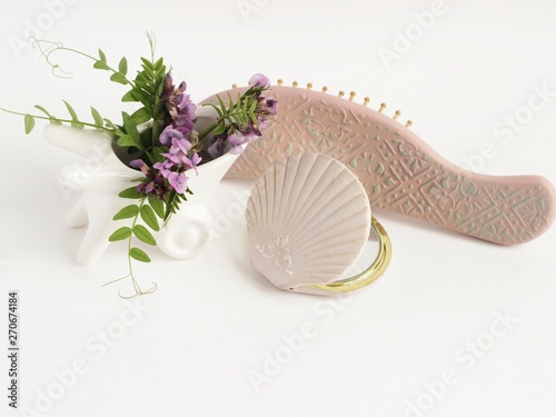 interiors, decor and beauty concept. home decoration. wildflowers sweet pea in a ceramic white pot in the form of a cart. a mirror and a comb handmade decor. white background. copy space for text photo