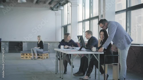 A male manager in a jacket walks around the office, communicates with colleagues, and gives them tasks. Coworking. Office workflow. Modern trendy office interior in a loft style