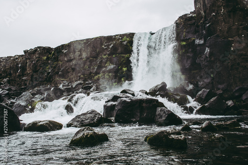 The waterfall of Öxarárfoss in Thingvellir National Park, Iceland flowing from the river Öxará into the pool filled with rocks. Cold cloudy weather in spring