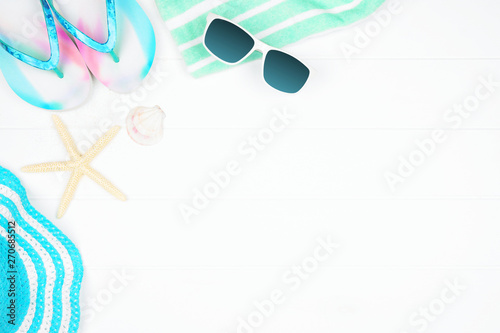 Beach accessories on a white wood background. Summer vacation concept corner border with copy space. Sunglasses, sea shells, towel, flip flops and blue striped hat.
