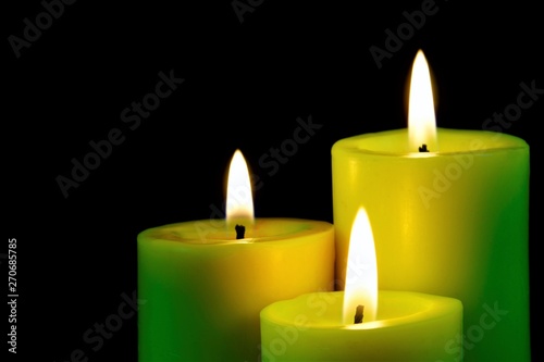 Bright candles burning on a black creative background. The candle illuminates, and a symbol of faith, hope, love, Christmas holiday and a significant event.