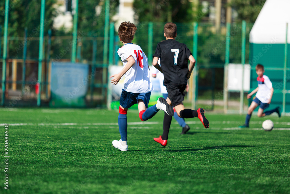 Boys at blue white sportswear run, dribble, attack on football field. Young soccer players with ball on green grass. Training, football, active lifestyle for kids Boys at blue white sportswear run, dribble, attack on football field. Young soccer players with ball on green grass. Training, football, active lifestyle for kids