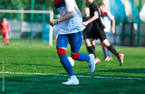 Boys at blue white sportswear run, dribble, attack on football field. Young soccer players with ball on green grass. Training, football, active lifestyle for kids 