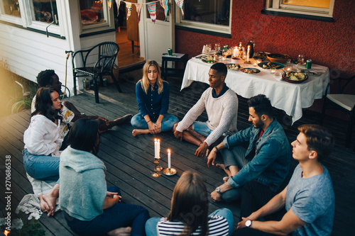 High angle view of male and female friends sitting with eyes closed around lit candles in balcony during group therapy s photo