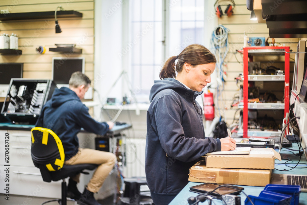 Tekniker antecknar vid arbetsbord medan kollega arbetar i bakgrunden