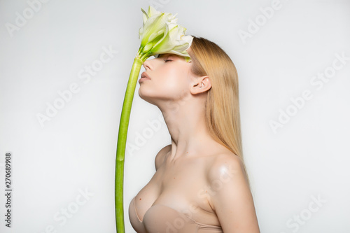 Half length portrait of a beautiful young, fresh, healthy woman with perfect skin that closed eyes with big white flower on her head, isolated against grey background