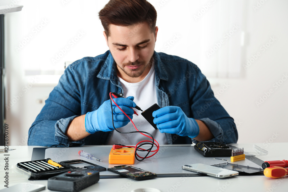 Technician checking broken smartphone at table in repair shop