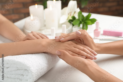 Cosmetologist massaging client's hand at table in spa salon, closeup