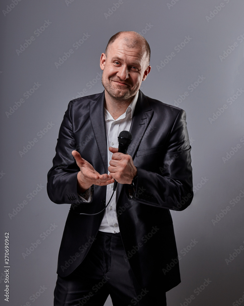 Fun emotional moving happy performer man presenting the show holding microphone in hand and showing the hand the welcome sign on grey color background. Fun emotional moving happy performer man presenting the show holding microphone in hand and showing the hand the welcome sign on grey color background.