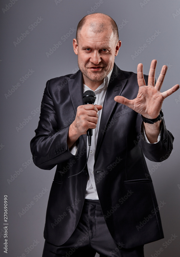 Excited happy crying performer man dancing and presenting the show holding microphone in hand on grey color background. Closeup Excited happy crying performer man dancing and presenting the show holding microphone in hand on grey color background. Closeup