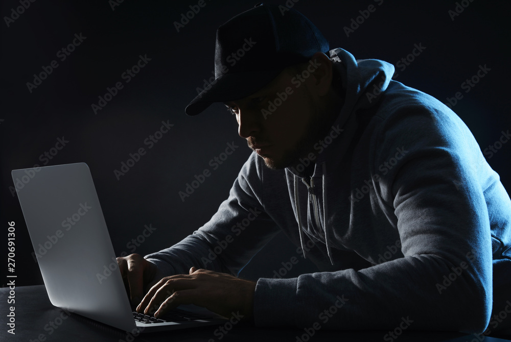 Man using laptop at table on dark background. Criminal activity Man using laptop at table on dark background. Criminal activity