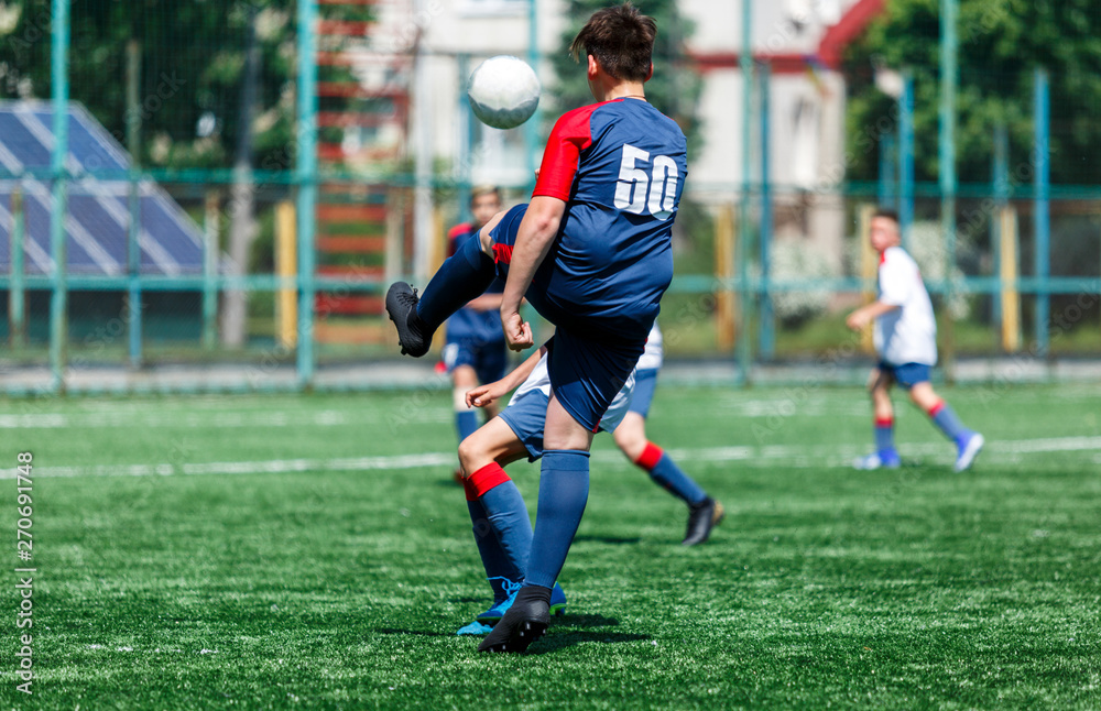 Boys at blue white sportswear run, dribble, attack on football field. Young soccer players with ball on green grass. Training, football, active lifestyle for kids