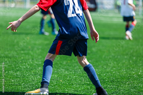 Boys at blue white sportswear run, dribble, attack on football field. Young soccer players with ball on green grass. Training, football, active lifestyle for kids
