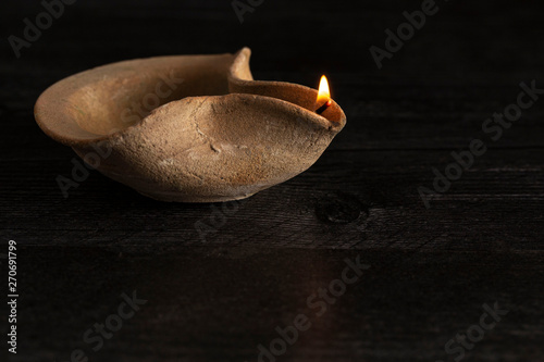 Картината върху платно A Lit Handmade Oil Lamp from the Middle East on a Dark Table