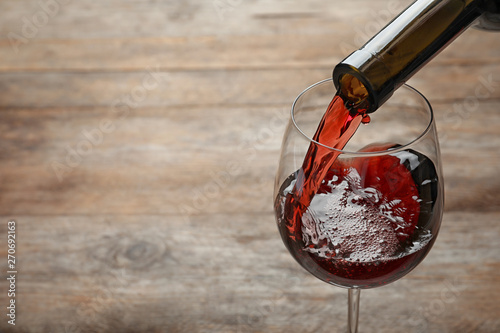 Pouring red wine from bottle into glass on wooden background. Space for text