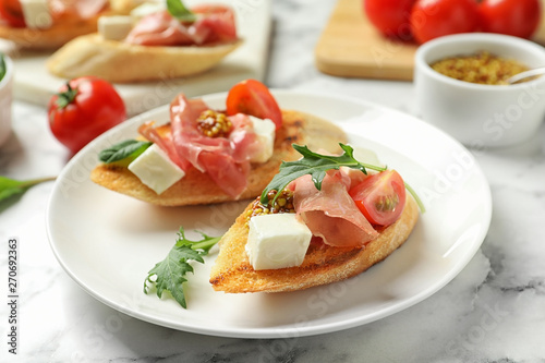 Plate of tasty bruschettas with prosciutto on table