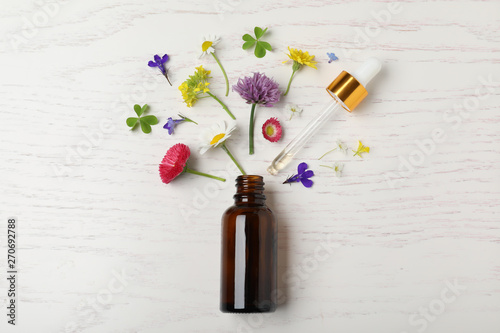 Bottle of essential oil and different flowers on white wooden background, flat lay photo