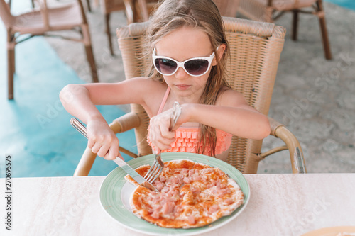 Portrait of cute little girl sitting by dinner table and eating pizza © travnikovstudio