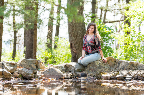 Woman in jeans sitting relaxing on rocks in sunny forest during spring in Mill Mountain park in Roanoke  Virginia by pond