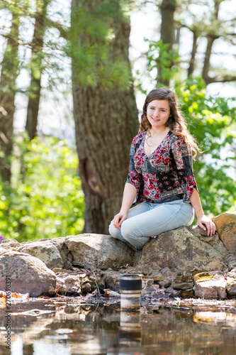 Happy woman sitting relaxing on rocks in sunny forest during spring in Mill Mountain park in Roanoke, Virginia by pond