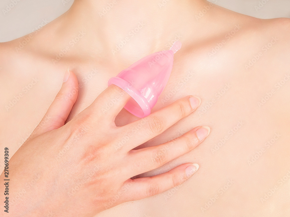 Fototapeta premium Close up of woman hand holding menstrual cup over her skin. Eco-friendly concept for women's health. Innovation product in gynecology that replaced traditional approaches.