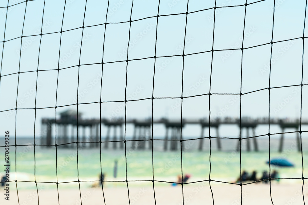 Fort Walton Beach, Okaloosa Island fishing pier in Florida, Panhandle Gulf of Mexico in summer with closeup view through beach volleyball net people in blurred background Fort Walton Beach, Okaloosa Island fishing pier in Florida, Panhandle Gulf of Mexico in summer with closeup view through beach volleyball net people in blurred background