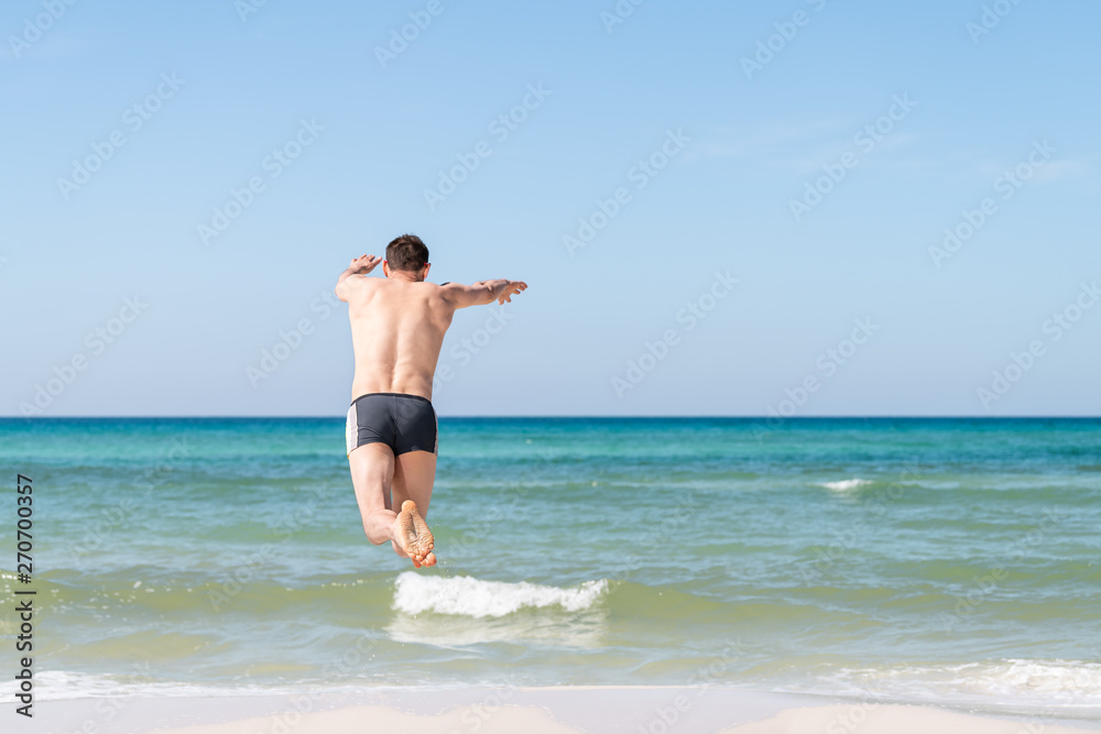 Back of young happy man jumping, diving plunging into ocean water mid-air with arms outstretched in summer in Santa Rosa Beach, Florida