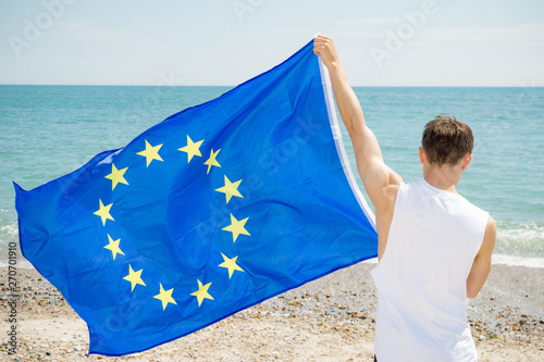 Caucasian male on a beach holding an EU flag
