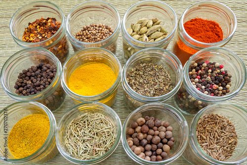Twelve different spices and herb seasonings in a glass jars on a rough green mat made of natural plant fibers. Natural food spices and seasonings. Tasty eating.