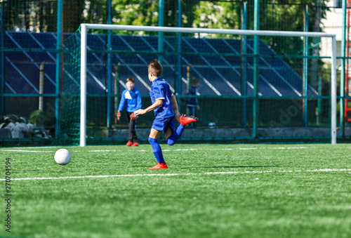 Boys at blue white sportswear run, dribble, attack on football field. Young soccer players with ball on green grass. Training, football, active lifestyle for kids © Natali