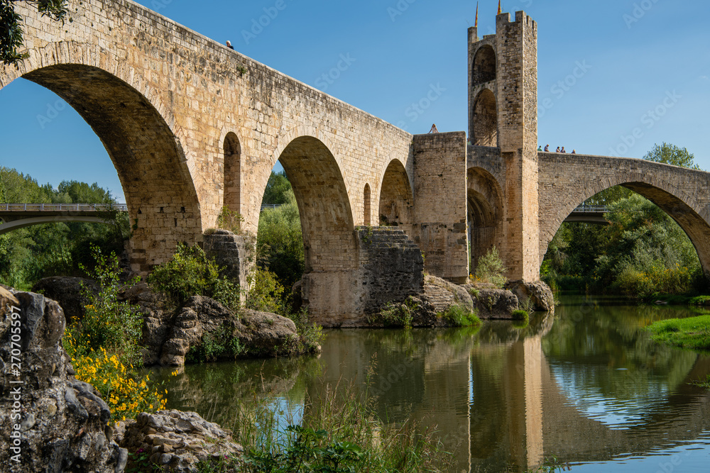 Girona, Spain - Sept 24 2018: View from under the romanesque bridge across Fluvia river with arches and defence towers in Besalu, Girona, Spain.