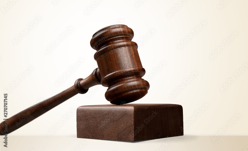 Male hand with wooden judge hammer, shelves with books on background Male hand with wooden judge hammer, shelves with books on background