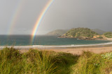 The end of a double rainbow over the deserted, sandy beach at Matai Bay, Karikari Peninsula, Northland, New Zealand.