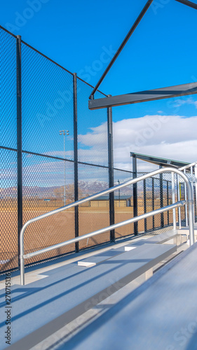Vertical frame Sunlit bleachers overlooking a vast sports field on the other side of the fence
