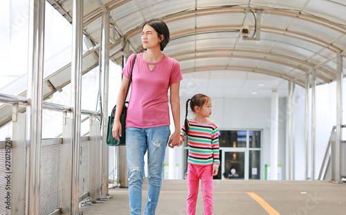 Asian mother holding hands her daughter walking on overpass. Mon and child girl walk together.