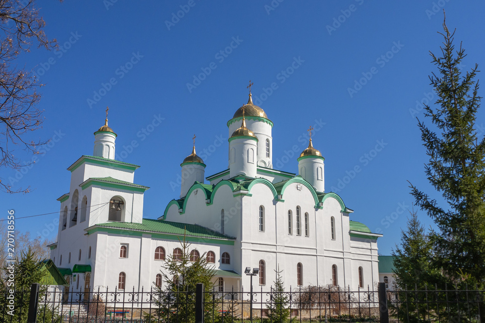 White, orthodox temple with golden domes against the blue sky.