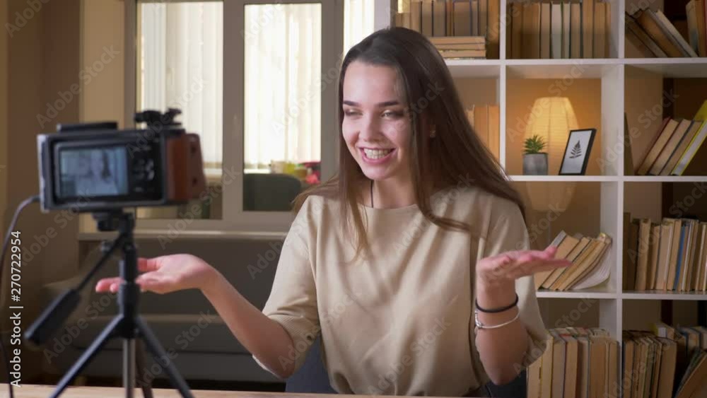 Closeup portrait of young attractive caucasian female blogger talking on camera and showing a thumb up indoors Closeup portrait of young attractive caucasian female blogger talking on camera and showing a thumb up indoors