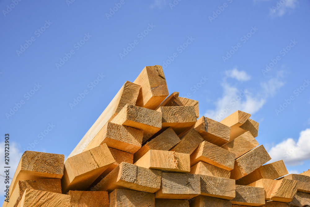 Fototapeta premium Stacked lumber on blue sky.Folded wood.Closeup wooden boards.The surface of the end of the board.Lots of planks stacked on top of each other in the warehouse.Lumber for use in construction.