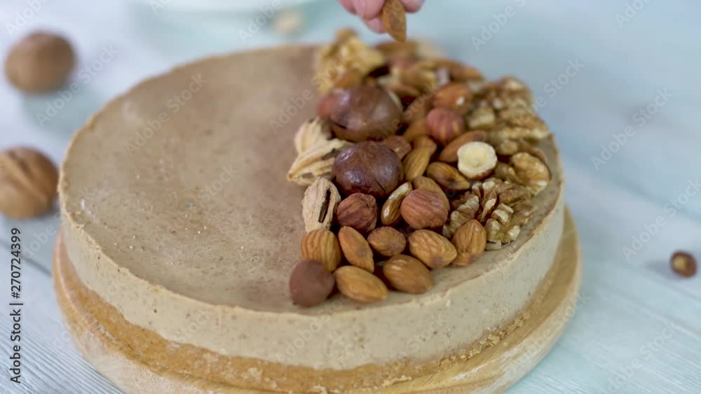 Nutty caramel cheesecake cake with topping of walnut, almond, hazelnut and macadamia on a wooden background. Confectioner in a blue apron decorated homemade nut dessert. Nutty caramel cheesecake cake with topping of walnut, almond, hazelnut and macadamia on a wooden background. Confectioner in a blue apron decorated homemade nut dessert.