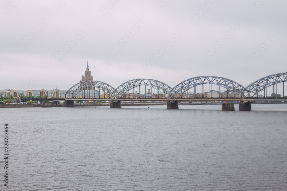 Naklejka premium City Riga, Latvian Republic. Railway bridge with river Daugava and buildings. Urban view. May 27. 2019 Travel photo.