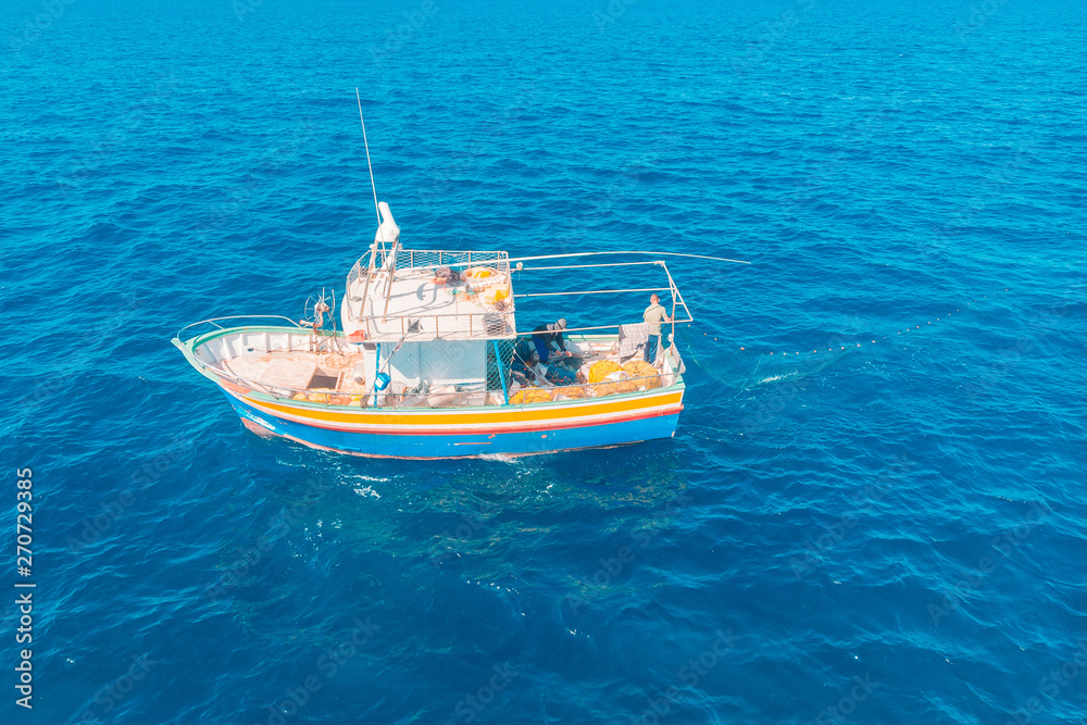 Fishing boat in blue sea water, fishermen set nets for fish. Aerial top view