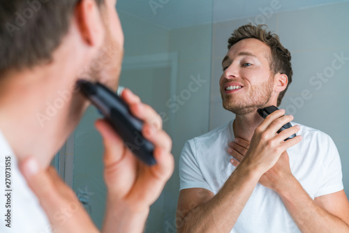 Young man shaving neck and jawline in the morning using electric shaver / clipper. Morning routine modern lifestyle. Male beauty 30s model.