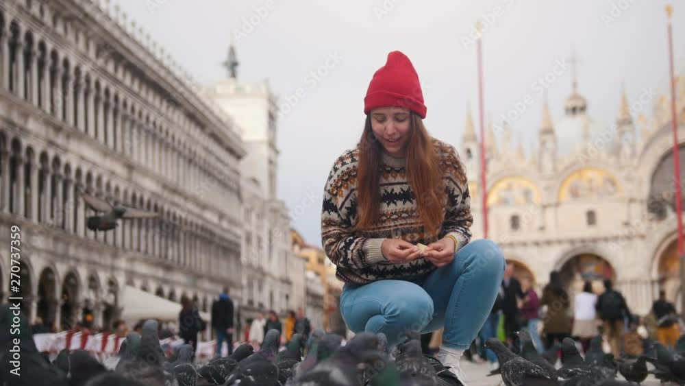 Young attractive woman squats in the square on the background of church and throws bread at a flock of pigeons Young attractive woman squats in the square on the background of church and throws bread at a flock of pigeons