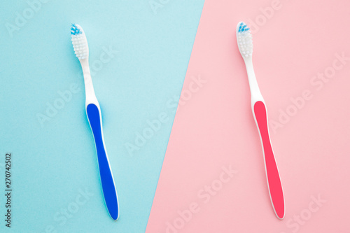 Two toothbrushes on pastel blue and pink background. Male and female teeth hygiene concept.