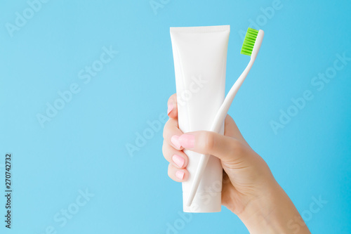 фотографія Woman's hand holding white tube of toothpaste and toothbrush with green bristles